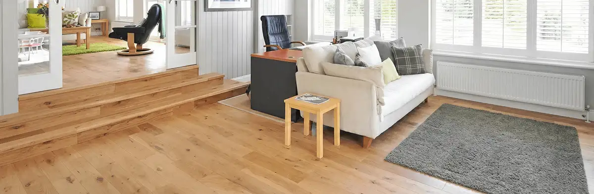 A modern living room with professionally installed laminate flooring, a beige sofa, a small side table, a gray rug, and large windows with white shutters in Akron, OH